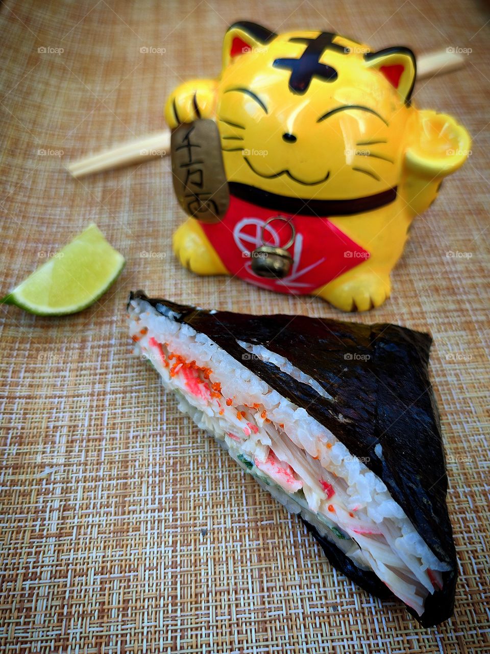 Composition. Sushi sandwich with crab. A piece of lime. Feng shui cat. Bamboo sticks. Asian cuisine