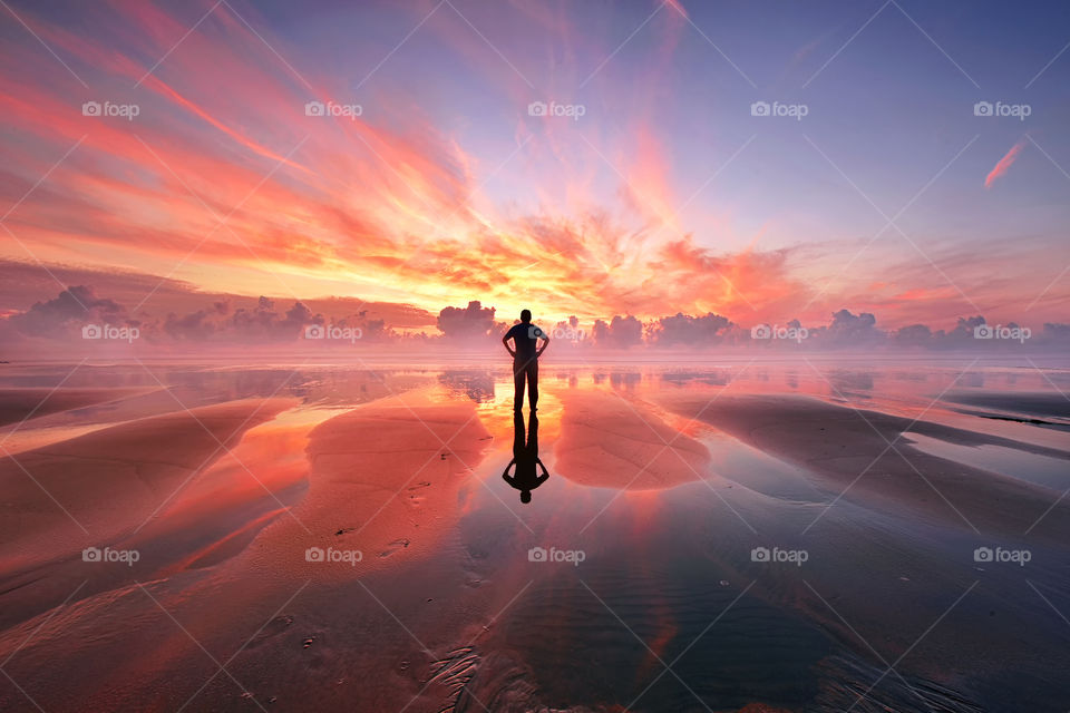 Silhouette man standing over the beach watching beautiful sunrise