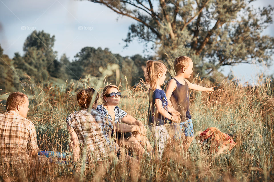 Family spending time together on a meadow, close to nature. Parents and children sitting and playing on a blanket on grass. Candid people, real moments, authentic situations