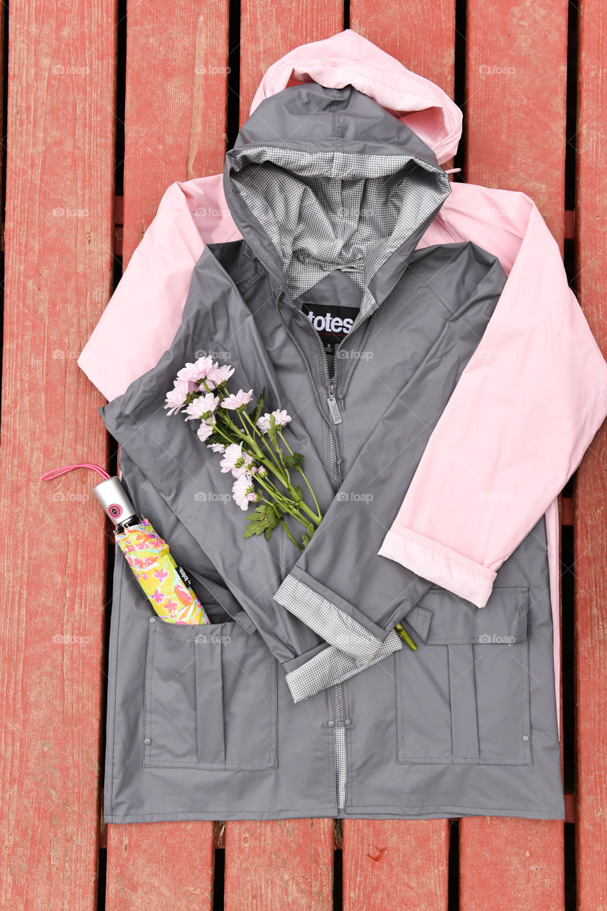 Flat lay of two raincoats with a bouquet of flowers and an umbrella