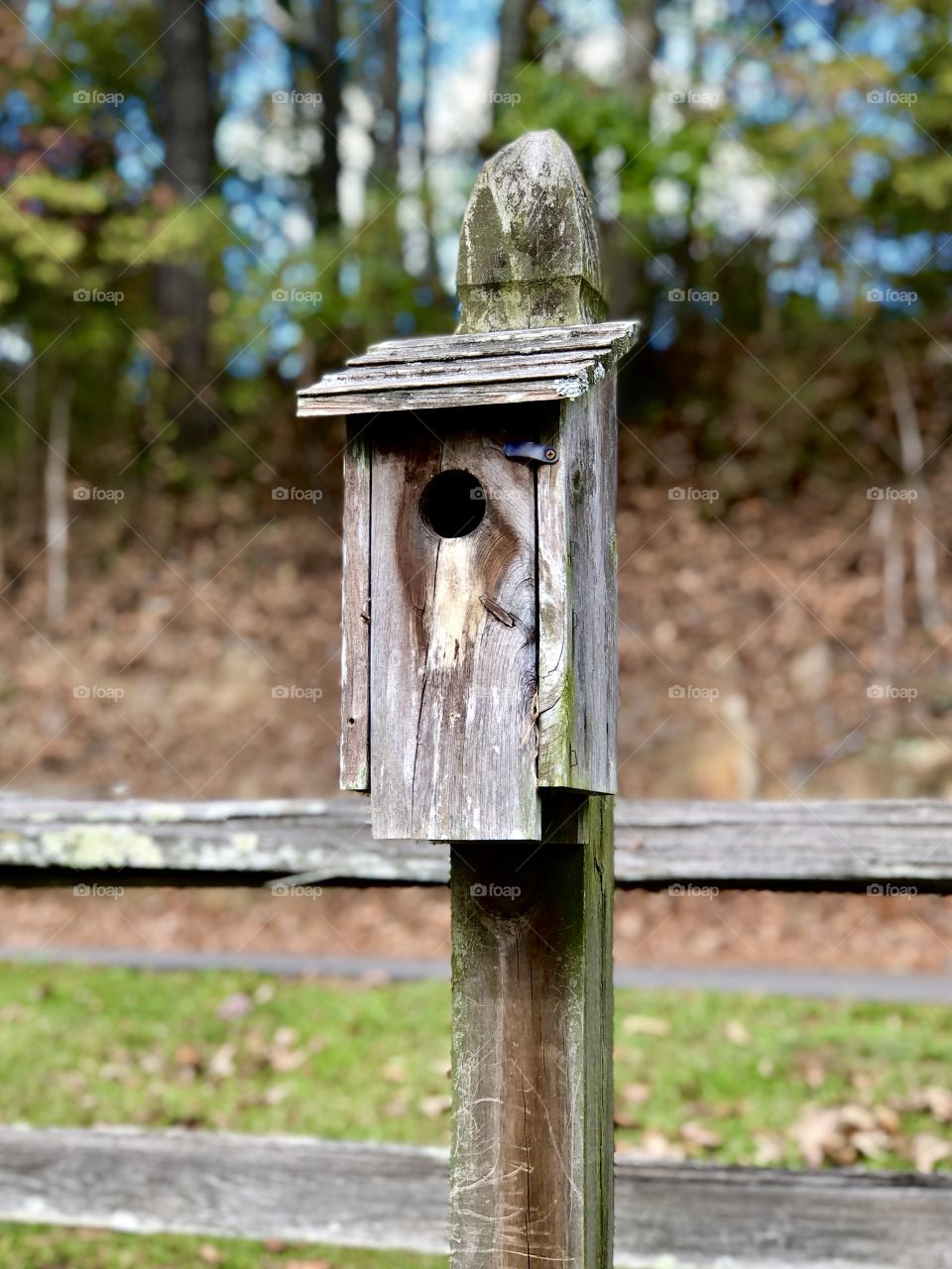 Wooden birdhouse on wooden post by rail fence