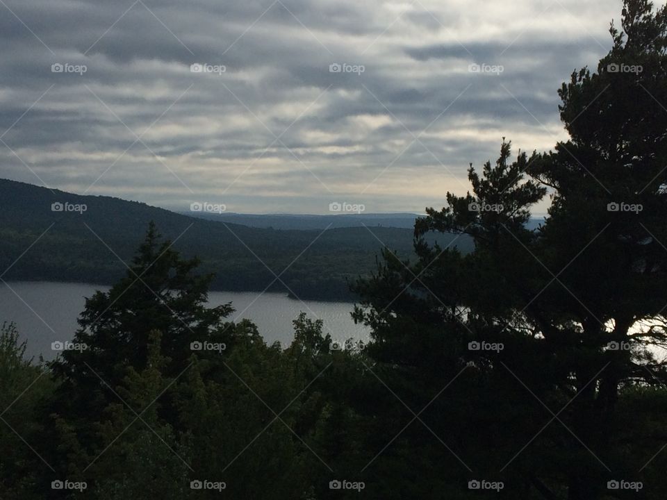 Tree silhouette with lake, mountains and cloudy sky behind