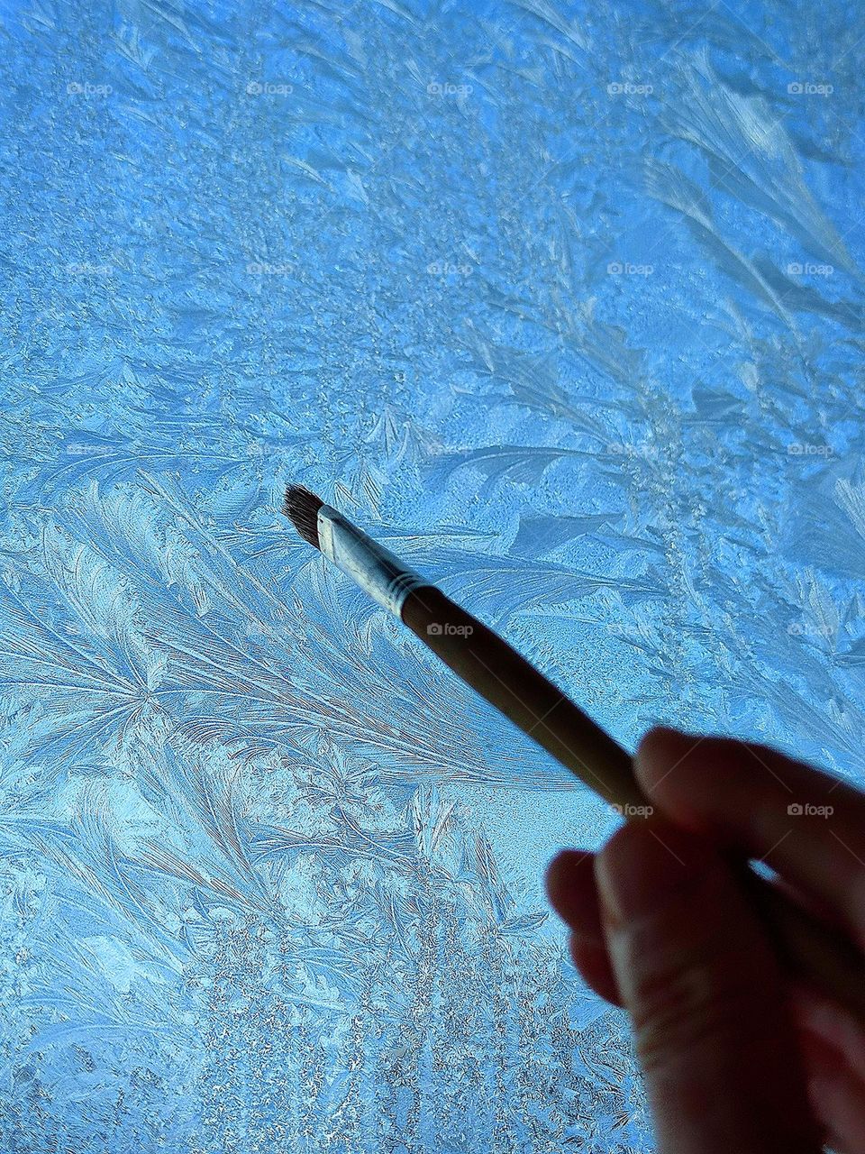 There is a pattern of frost on the glass.  The hand holds a brush "drawing" patterns