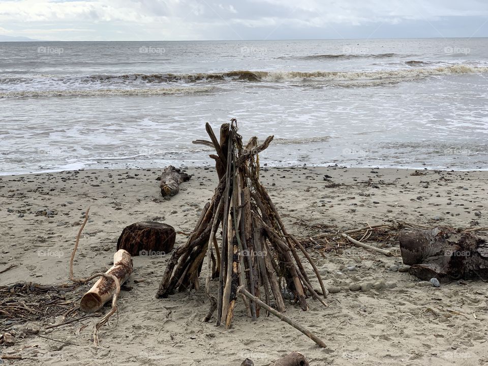 A tent of sticks on a beach during a beautiful winter day.