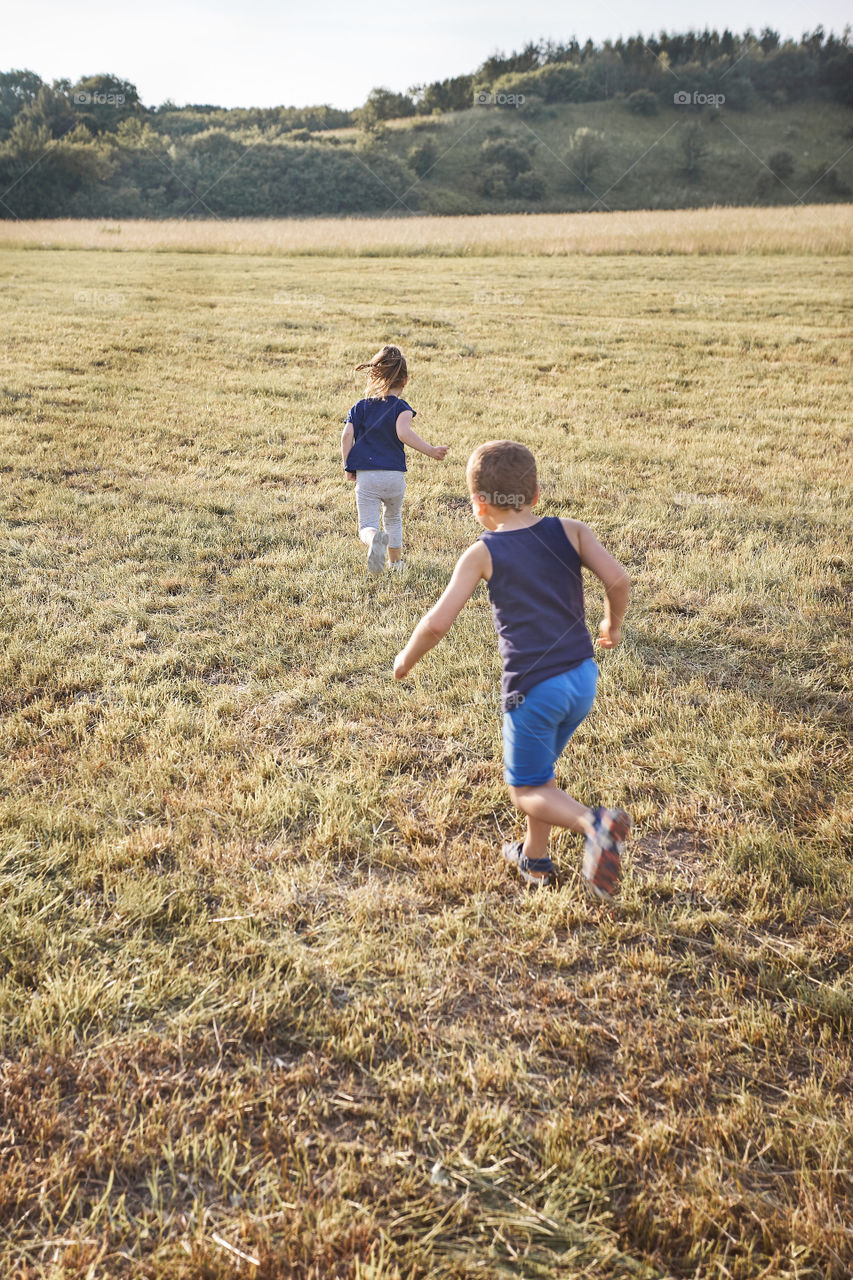 Children running through a field. Little girl and boy playing in the countryside. Candid people, real moments, authentic situations