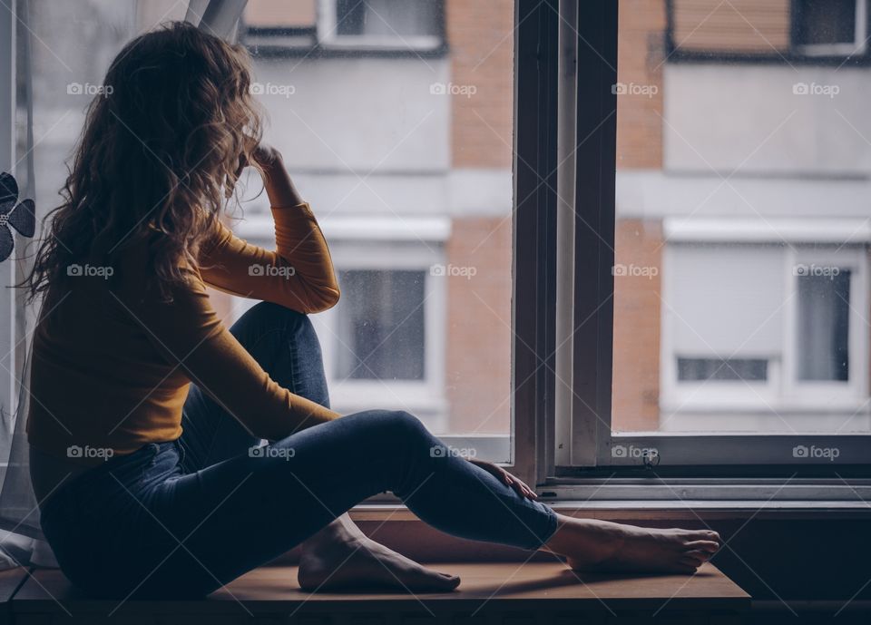 A girl sitting next to a window watching the rain. Nostalgia. Cold autumn days with heavy rain.