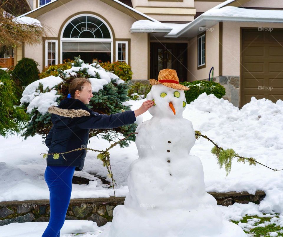 Girl makes snowman in snowy neighbourhood 
