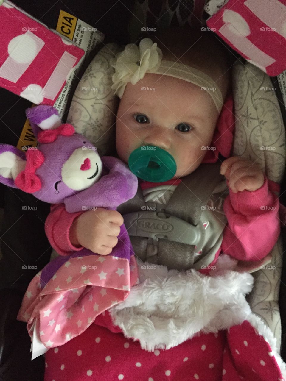 A little girl is all buckled into her carseat and snuggled up with her toy, ready for a little adventure 