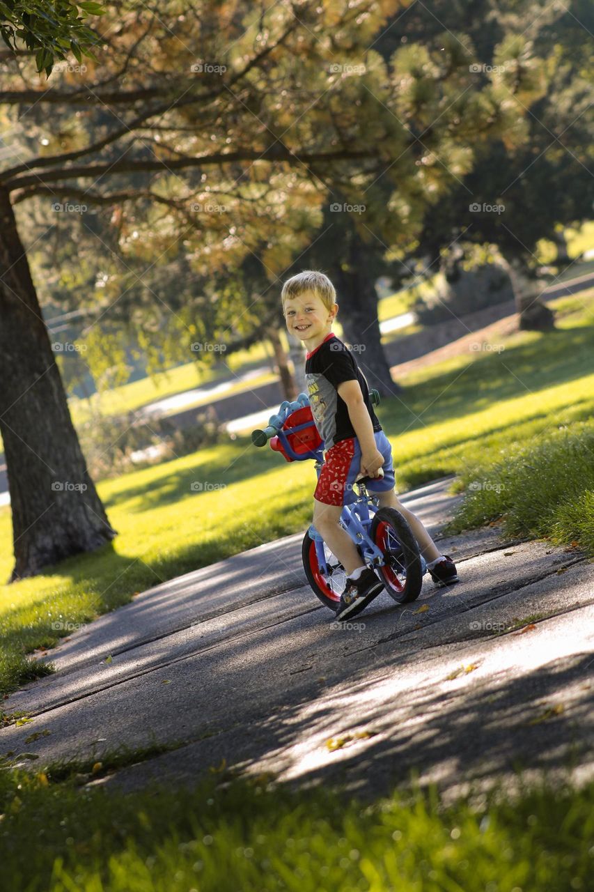 Little boy smiling riding his bike in the park in the fall 
