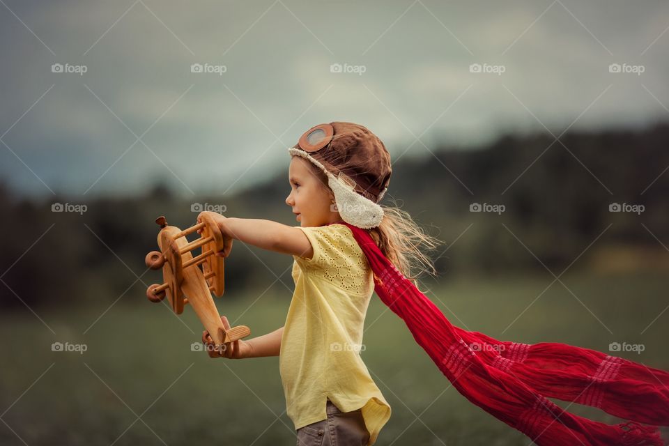 Little Aviator girl with wooden plane outdoor