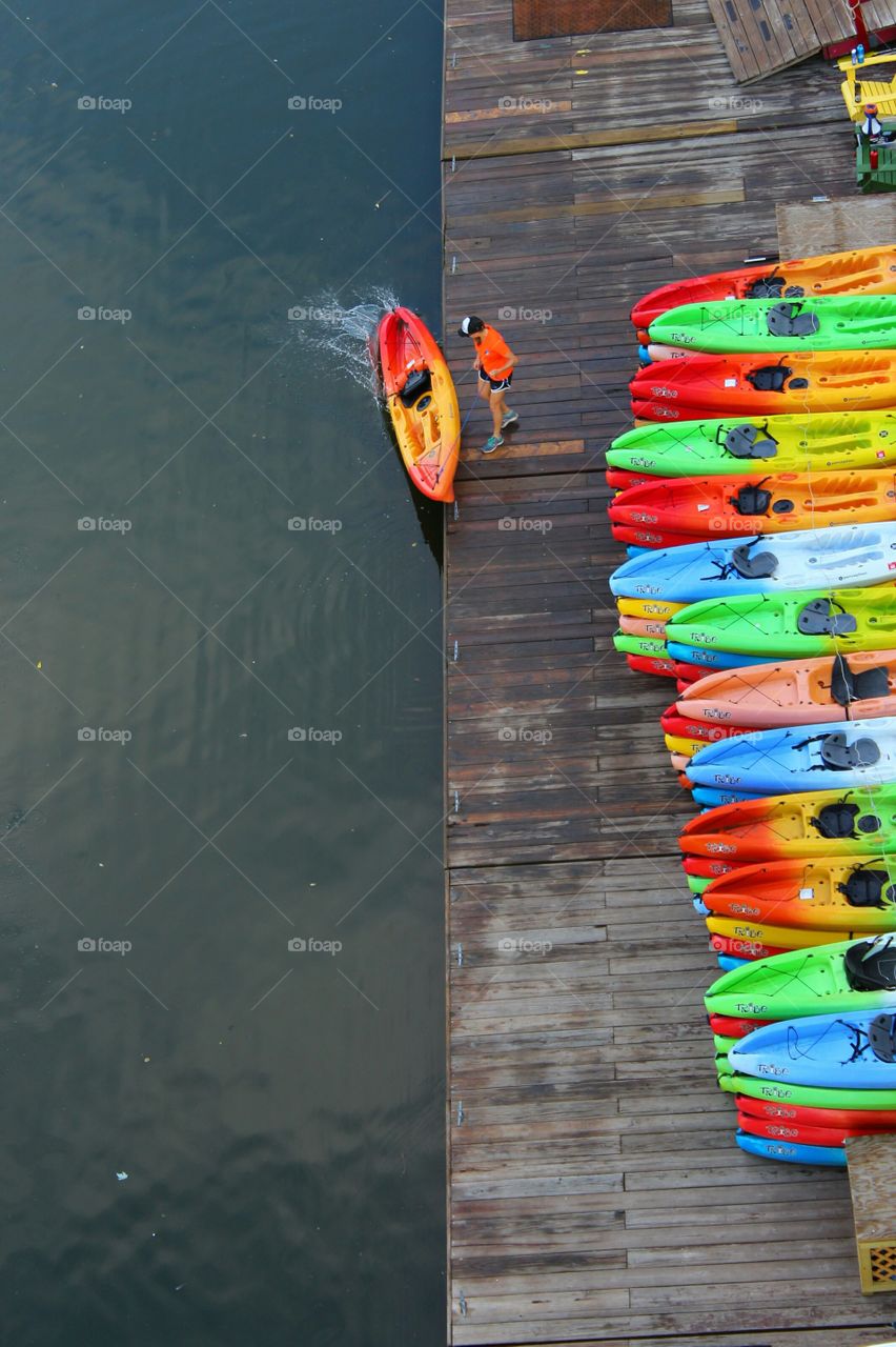 Stacks of neatly arranged colorful kayaks on a pier and one splashing into the water