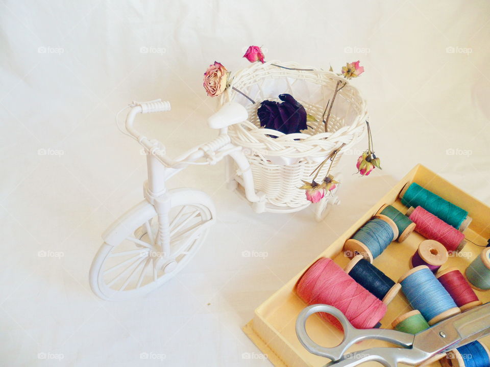 decorative toy bike, dried rosebuds and thread on white background