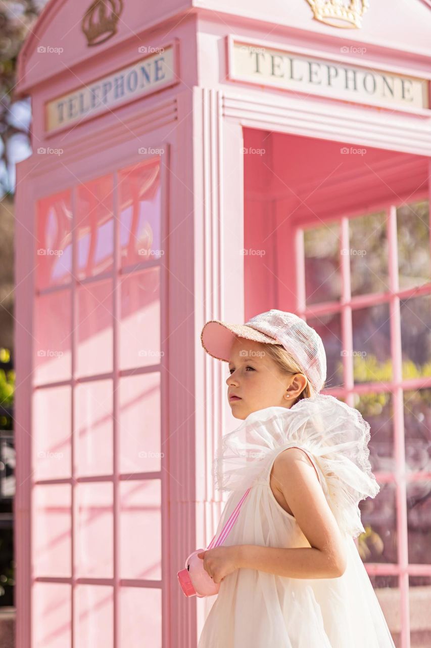 Cute little Caucasian girl near pink telephone booth 