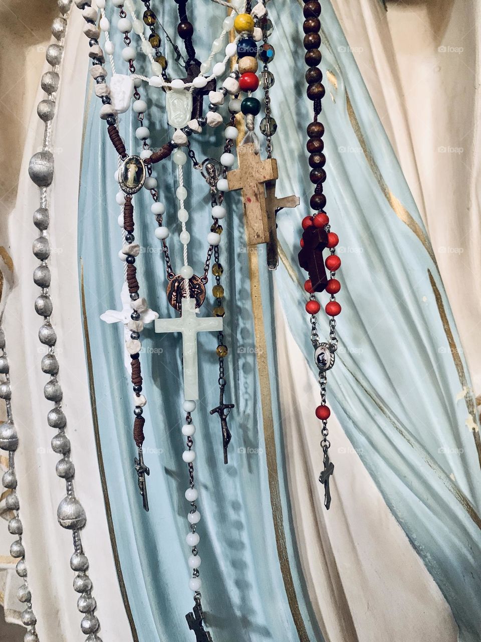 A statue depicting the Madonna who is entrusted with prayers and vows through the rosaries that are hung on her hands. Detail