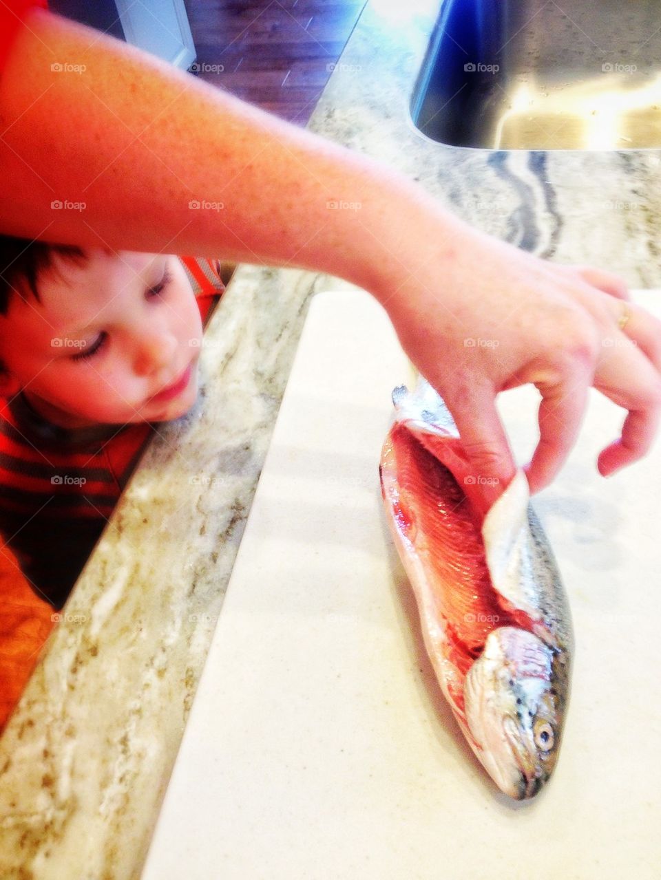 Learning How To Cook Fish. Boy Learning From Mom How To Prepare Fish
