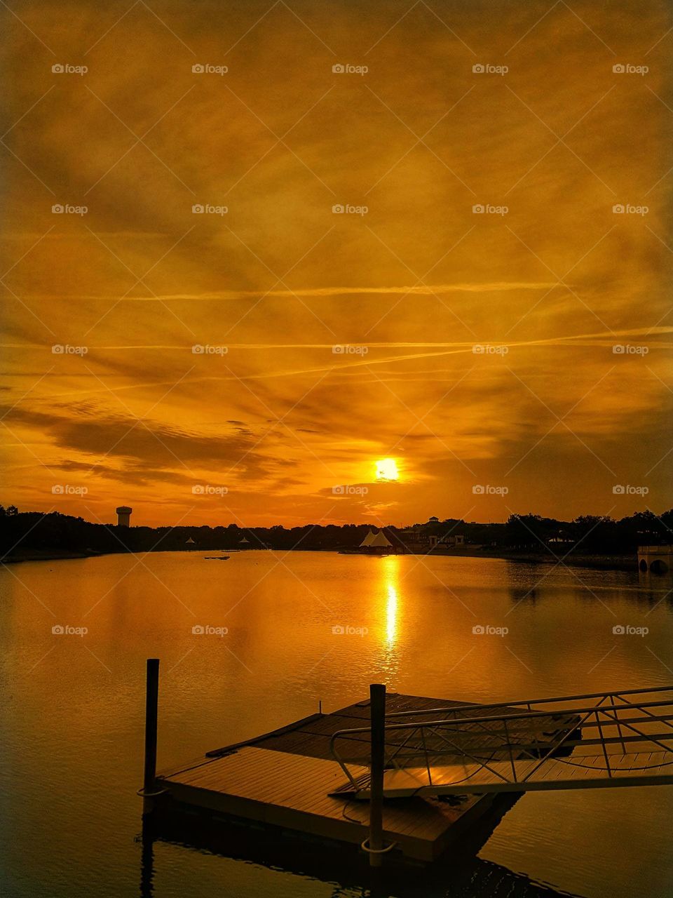 A golden orange sunrise above the lake and showing the dock at Cranes Roost Park in Altamonte Springs, Florida.