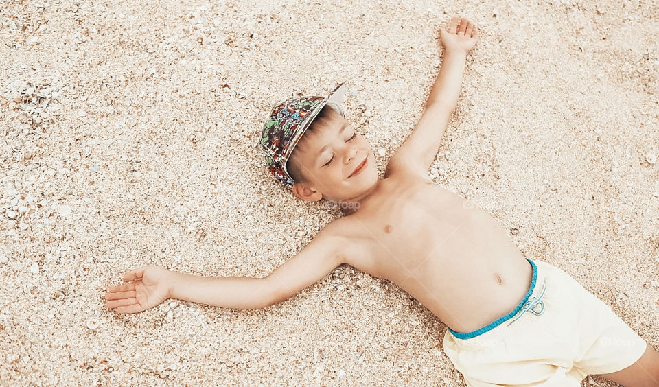 Smiling cute boy lying on a sandy beach 