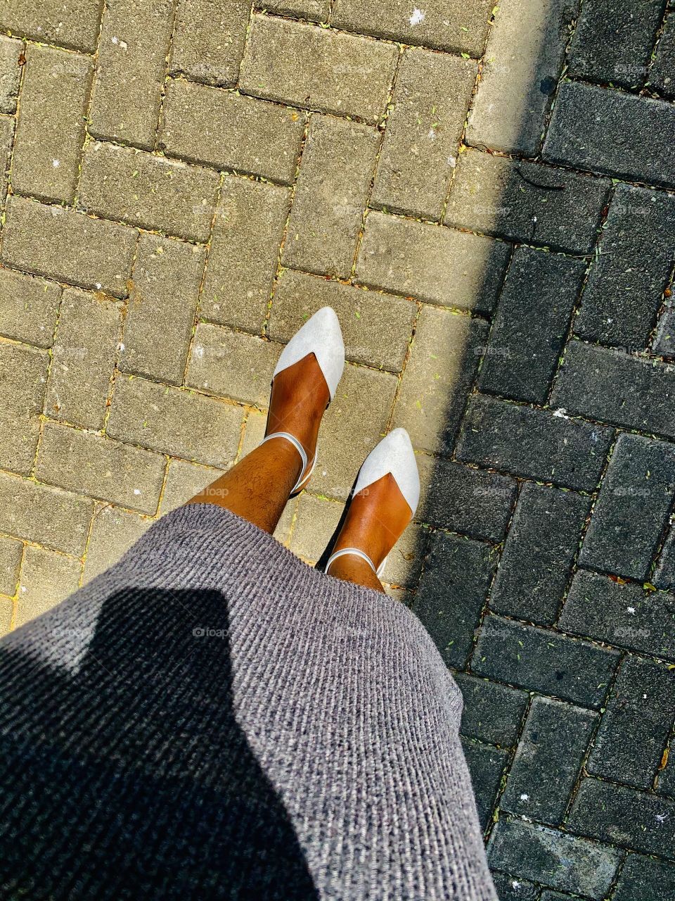 Legs of a black woman in a below knees long bandage dress and ankle strap flats on an interlocked pavement.