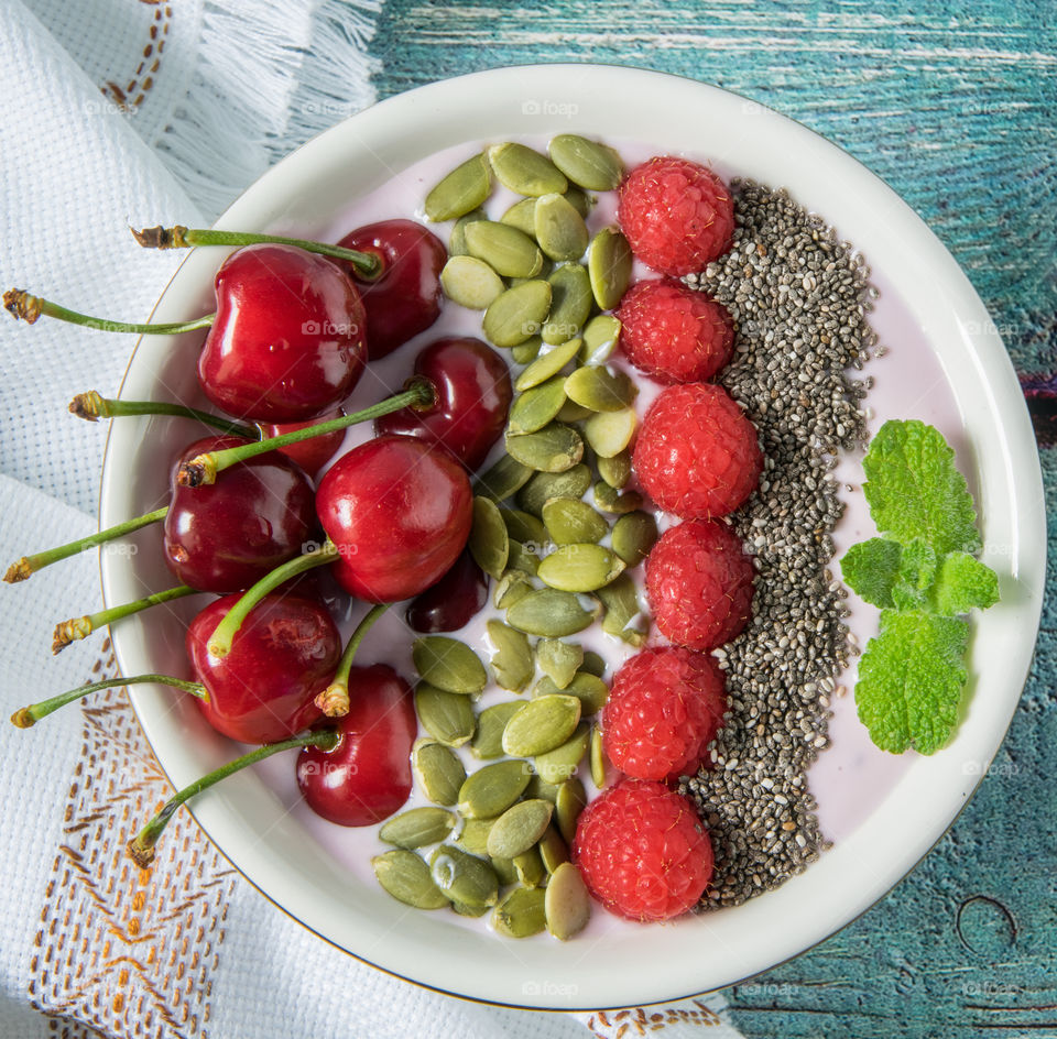 Yoghurt, banana and strawberry smoothie topped with cherries, raspberries and seeds