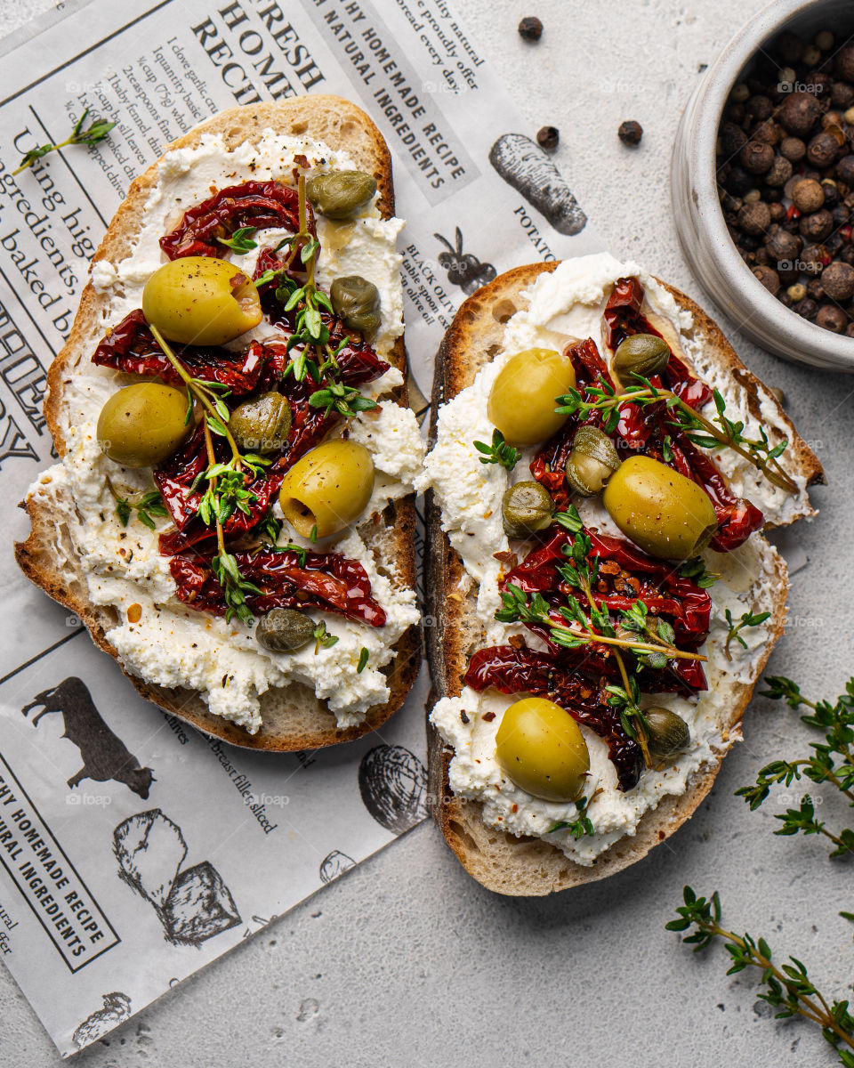 Two toasts with cream cheese, sun dried tomatoes and olives, top view