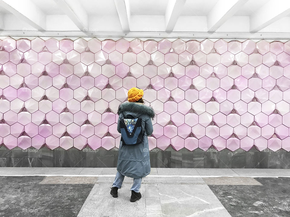 Young woman with a backpack standing in front of wall with geometric pattern 