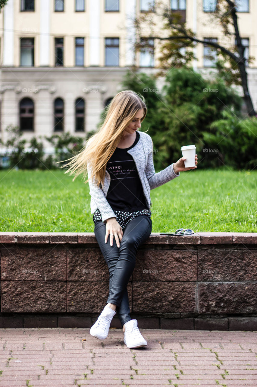 Woman sitting on retaining wall with glass on coffee in hand