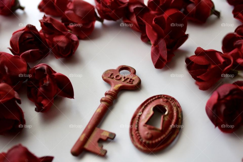 Red, metal, vintage key and keyhole with red, silk rose buds on white marble surface
