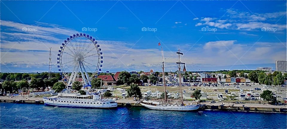 This is “Warnemünde”, a formerly “E German” harbor town by the “Baltic Sea” near “Rostock”. It is summertime and the “Ferris wheel” is in operation by the city port. 2022. Hypnotic Productions