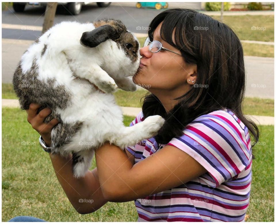 Young girl holding her pet rabbit , giving him a big kiss.