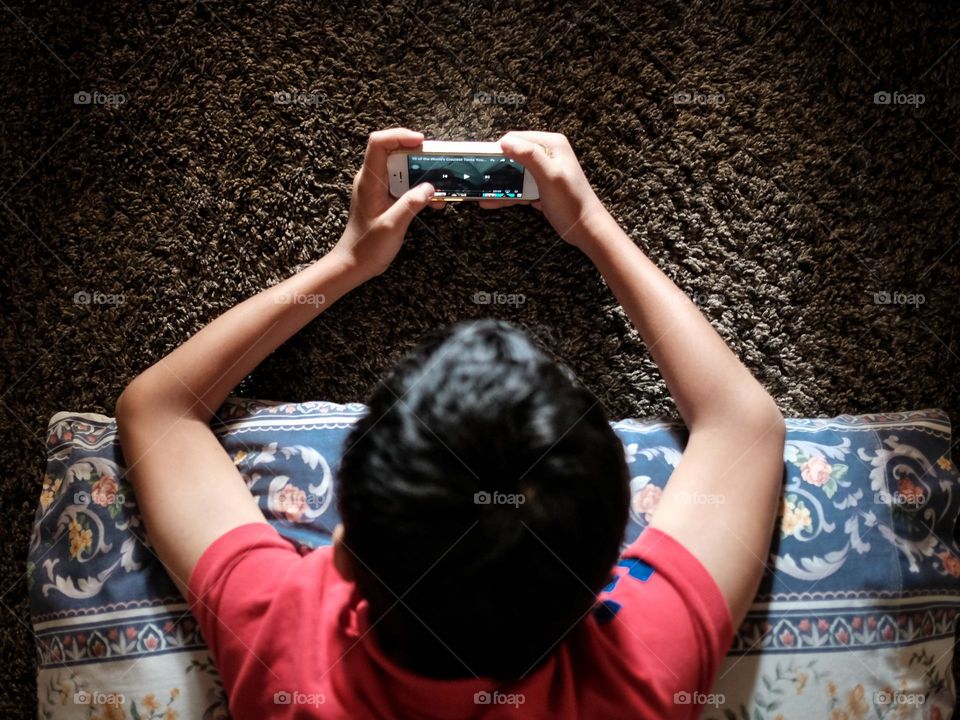 Top view of a boy on the carpet watching movies on his iphone