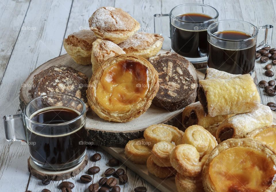 A selection of Portuguese pastries with black coffee on pale wooden background 