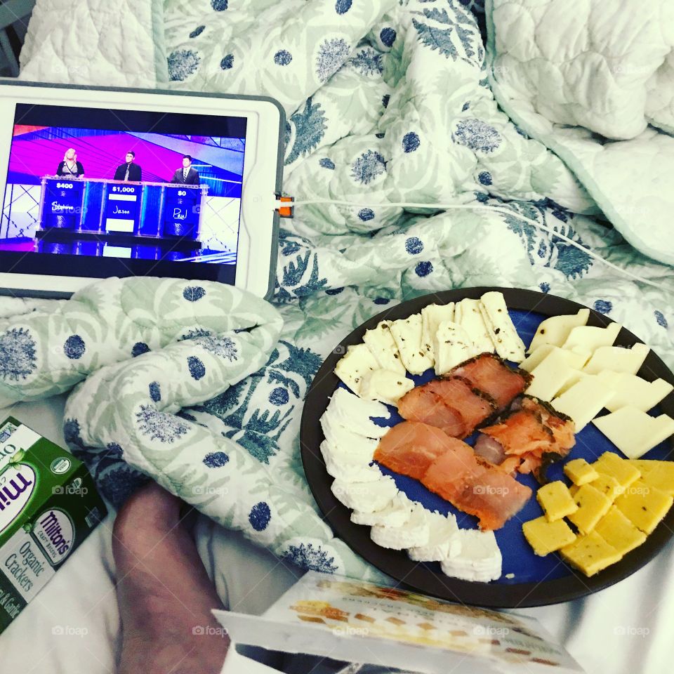 A plate of smoked salmon and assorted cheese with Jeopardy playing on an iPad 