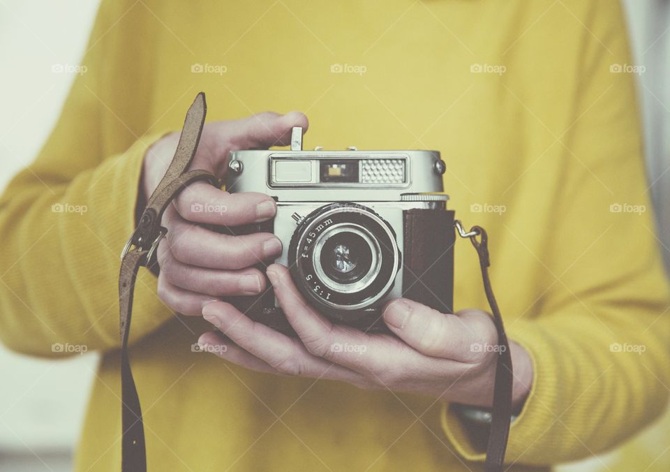 A midsection of a female photographer wearing yellow and focussing the lens of a vintage, 35 mm camera