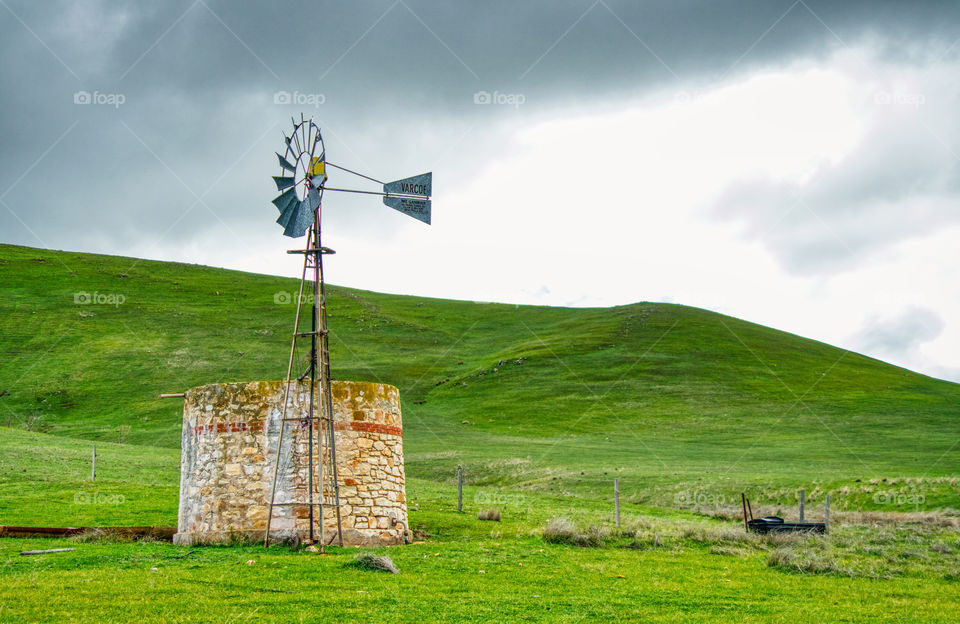 Windmill and stone tank of a green hill with a stormy sky. 