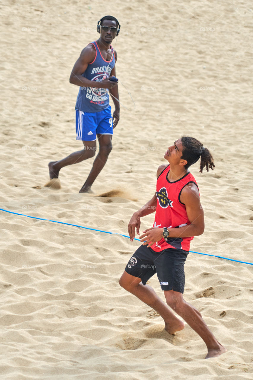 Man playing Footvolley being observed by a running man. 