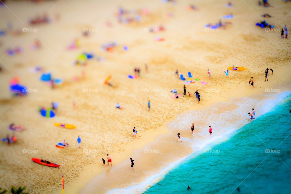 A busy sandy beach and emerald green ocean from above. Families and friends enjoying activities on a large beach.