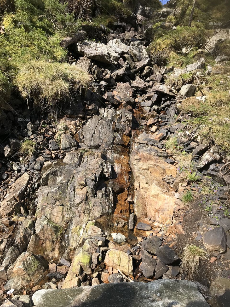 A water stream down a mountainside in Norway with grass and rocks around it.                                                                                          