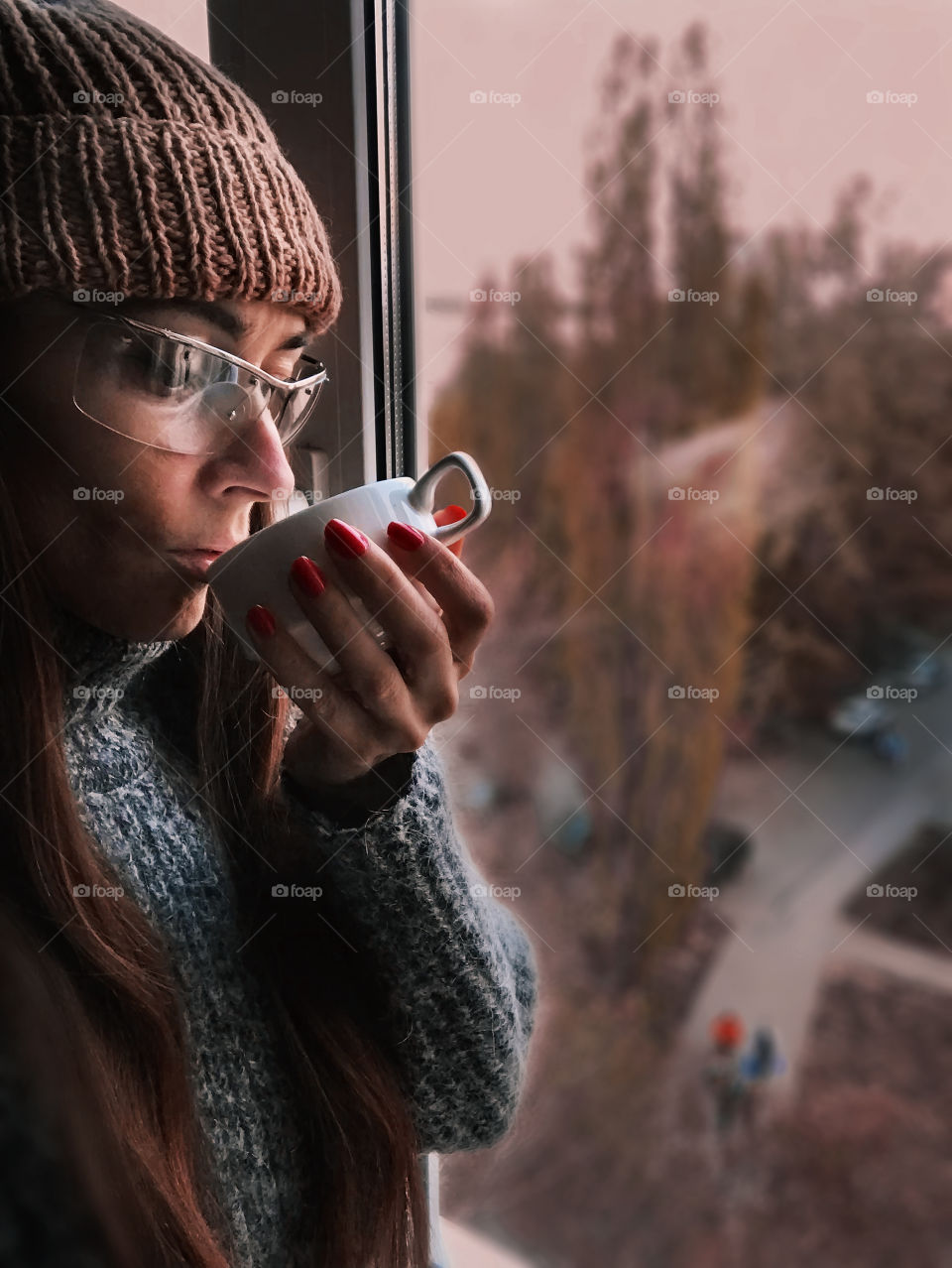 Young woman enjoying coffee in knitted sweater at the window 