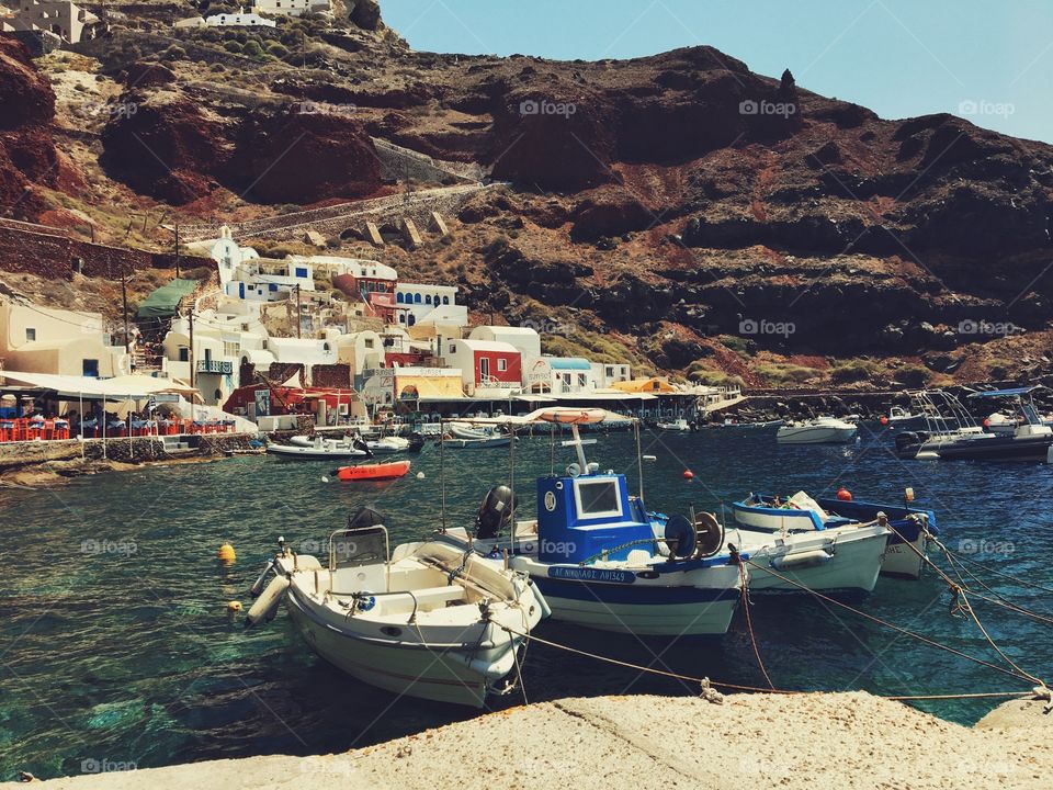 Little boats on the sea in Santorini, around white houses and rocky mountains.