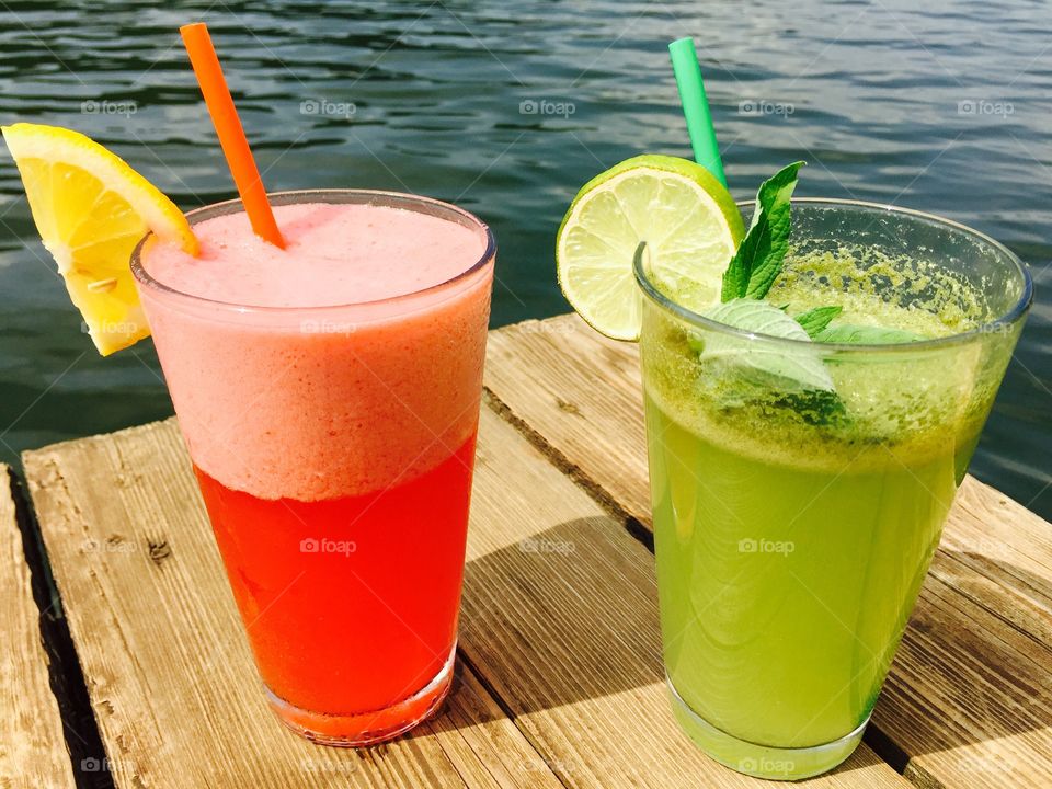 Strawberry lemonade and mint lemonade glasses near the lake