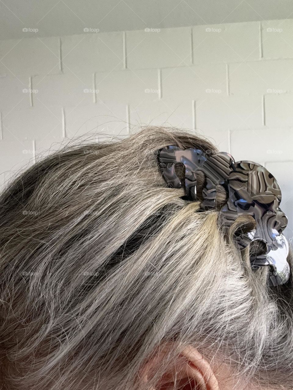 Woman with grey hair in bun using opalescent plastic claw clip