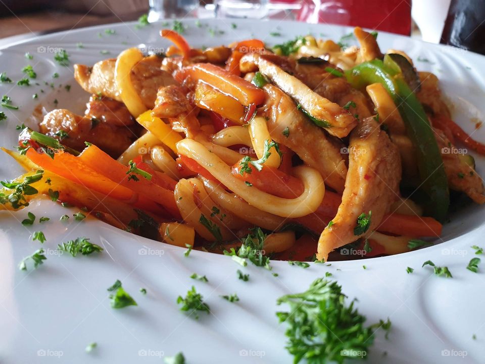 a delicious portrait of a tasty dish of noodles with chicken in a white plate in a restaurant.