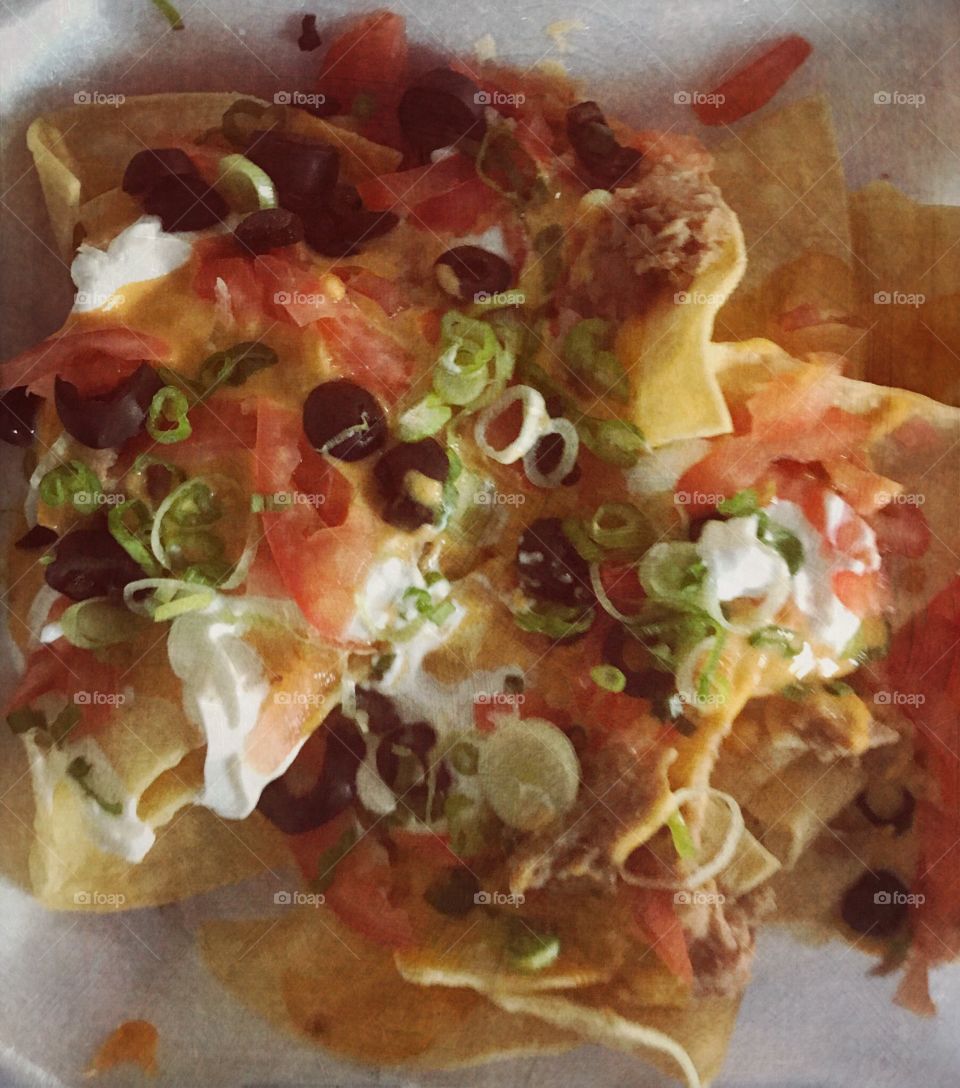 A delicious vibrant and colorful plate of nachos with olives, sour cream, cheese, onions, guacamole, and tomatoes. USA, America
