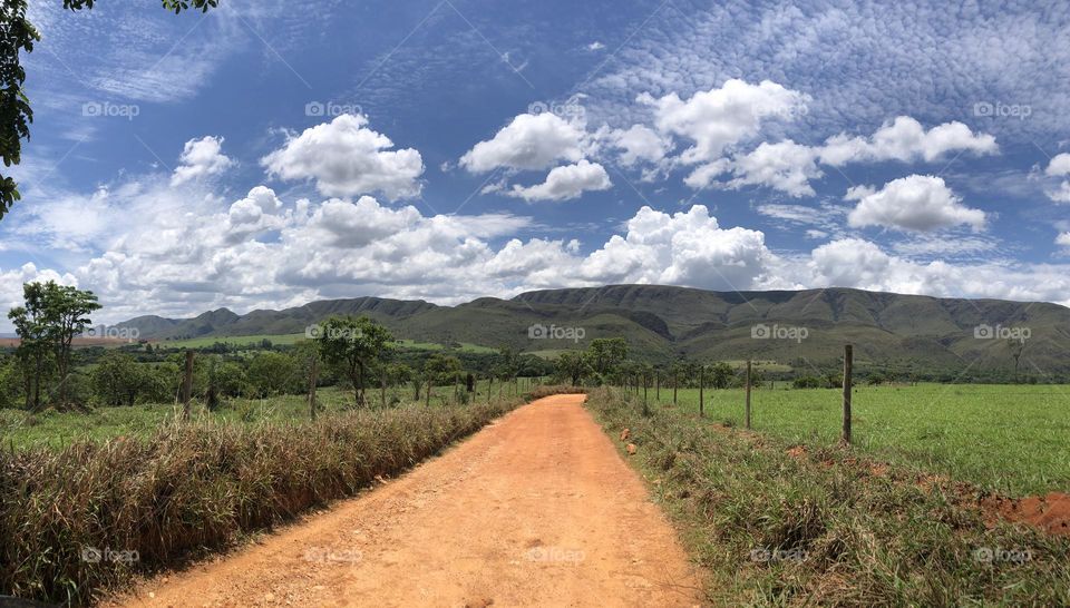 Empty dirty road going to the mountain and a cloudy blue sky 