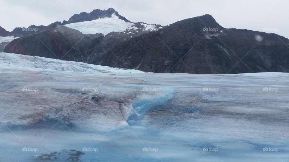 On top of Glacier in Alaska, an excursion in Juneau, blue and white ice with mountains behind