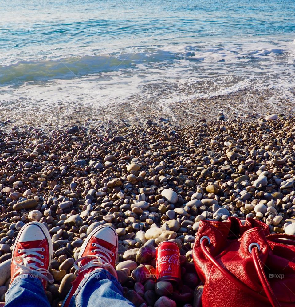 A can of Coca Cola on the beach with red sneakers and red leather bag.