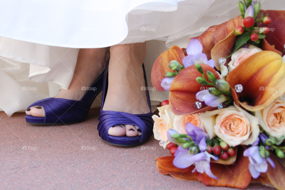 A bride's shoes peek out from under her dress next to her colourful bouquet