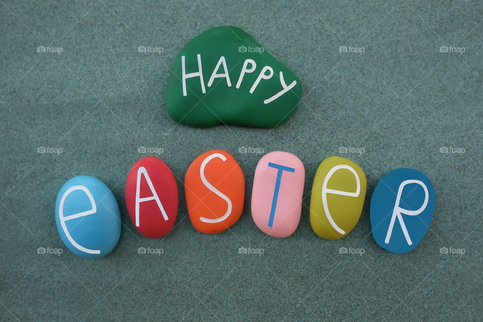 Happy Easter with colorful handmade painted stones over green sand