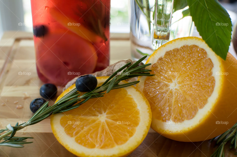 Making fresh homemade juices and refreshing gourmet detox drinks and flavored water with sliced orange, blueberry, citrus, cherry, raspberry, Rosemary and mint leaves