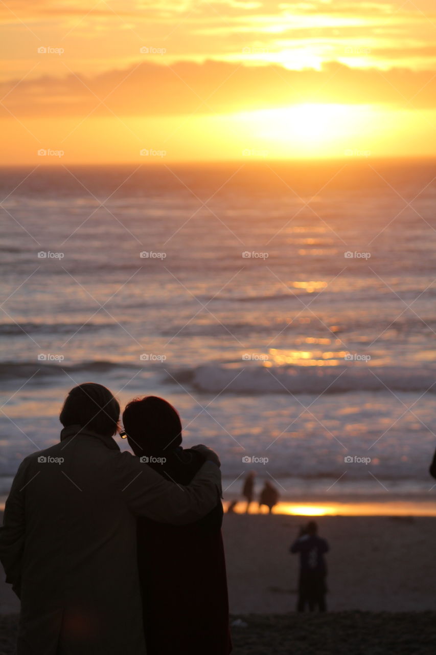 A couple takes on the sunset on the California coast.